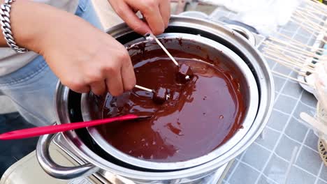 las manos sumergiendo golosinas en la olla de fondue de chocolate