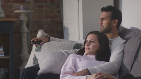 couple lying and relaxing on lounge sofa at home and watching horror film on tv together