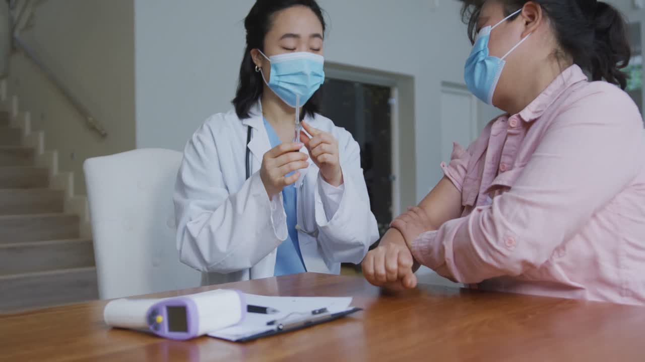 Asian female nurse wearing face mask preparing covid vaccination for female patient in hospital