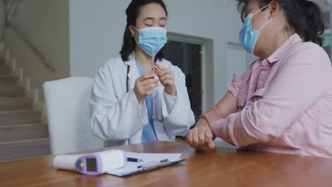 asian female nurse wearing face mask preparing covid vaccination for female patient in hospital