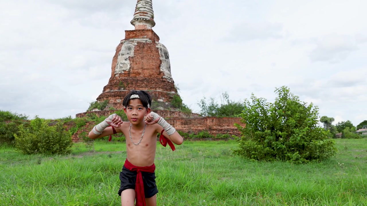 古代の石のパゴダの近くで、若いタイの少年が屋外で武術の動きを披露している。