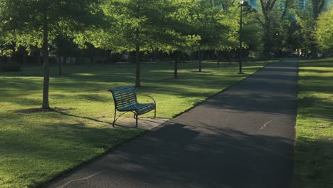 empty park bench in green park looking down empty walking path wide shot