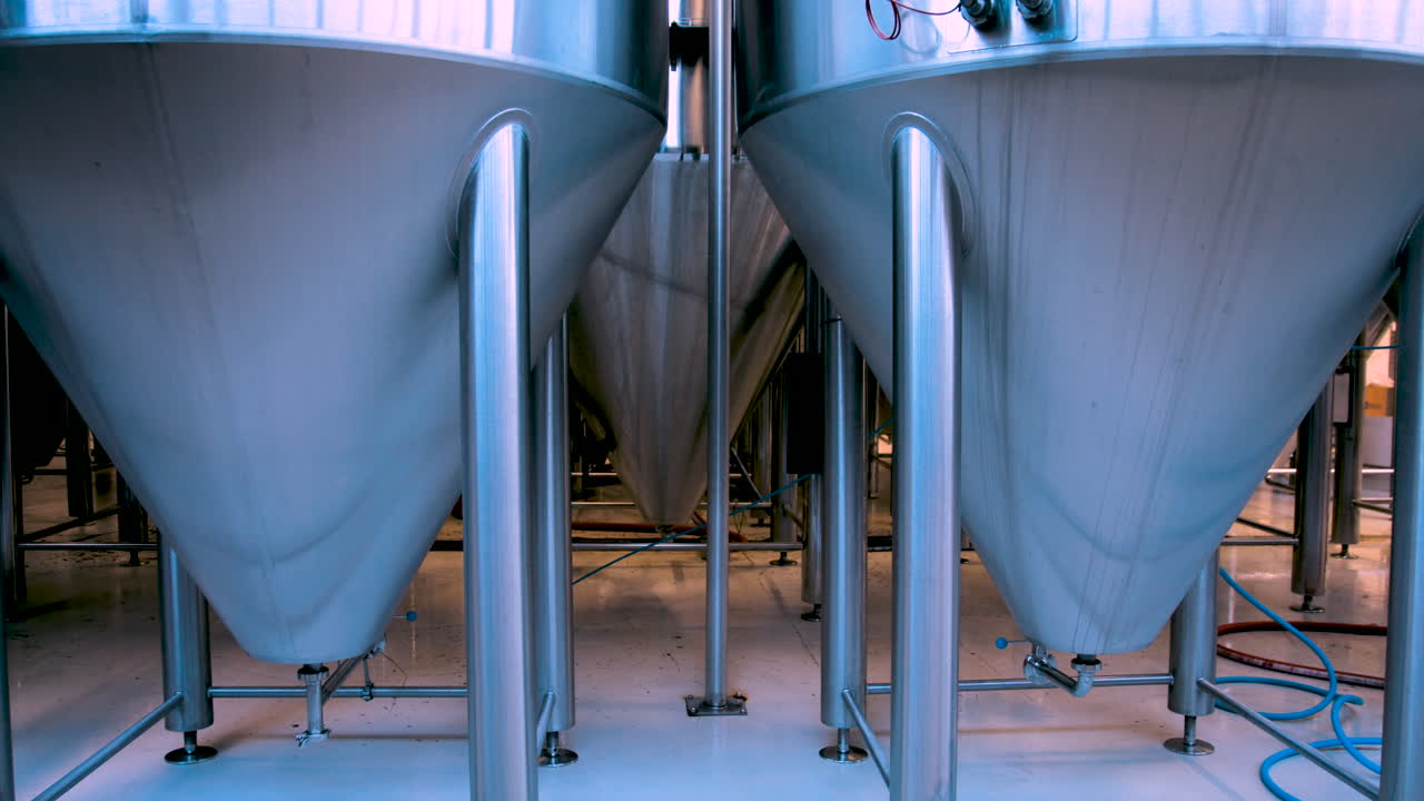 Steady shot of large stainless steel beer fermentation tanks in a brewery to with an indistinct shape walking in the background