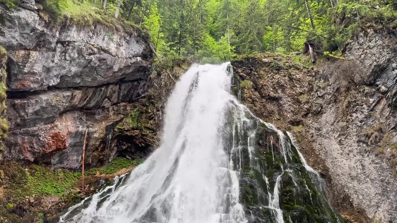 Vidvinkelbilde av Gollingfossen som fosser over lagdelt stein ned i et mørkt basseng, med skogkledde klipper, hvit sprut og filmatisk alpinstyrke.