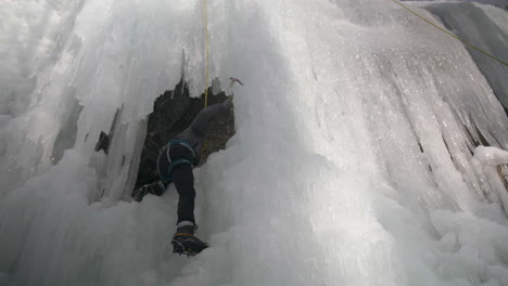 climber uses ice picks to climb onto a ledge , located on a large ice wall