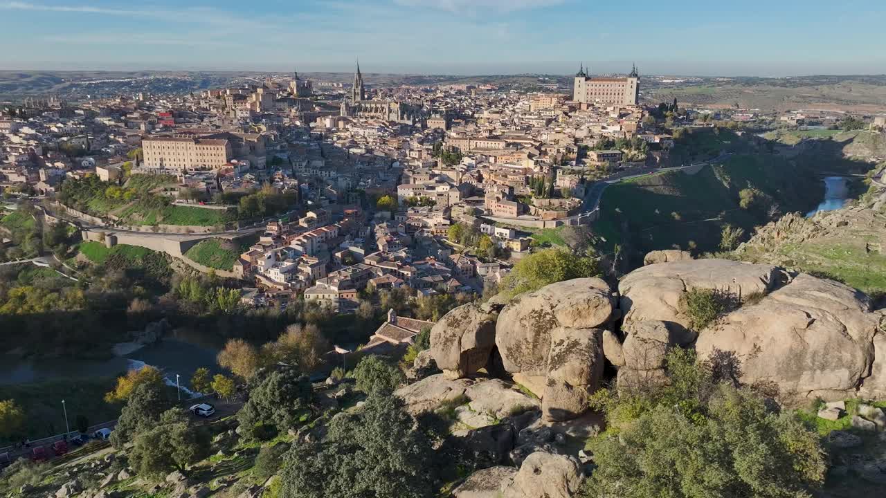 Nouseva dronelento oikealla panoroinnilla, joka näyttää upean panoraamanäkymän Toledoon, Espanjaan. Tagus-joki ympäröi historiallista kaupunkia katedraalinsa, Alcázarinsa ja siluettinsa kanssa sinisen taivaan alla.