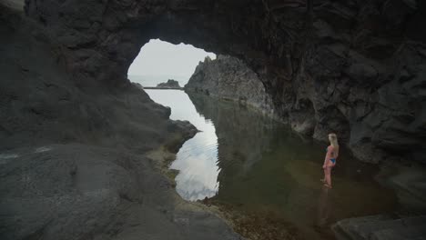 Female-tourist-in-blue-bikini-standing-at-rock-steps-of-natural-ocean-pool,-Seixal