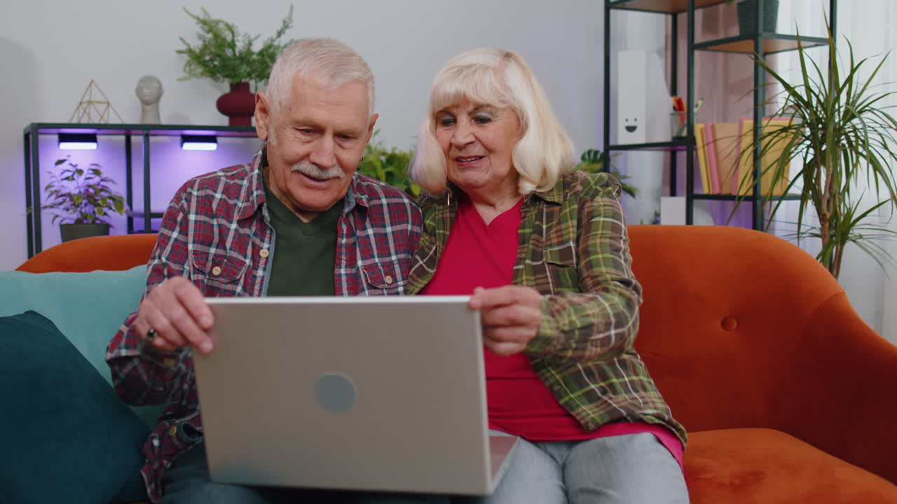 abuela mayor abuelo usando computadora portátil, escribiendo en la habitación de casa, mirando a la cámara sonriendo