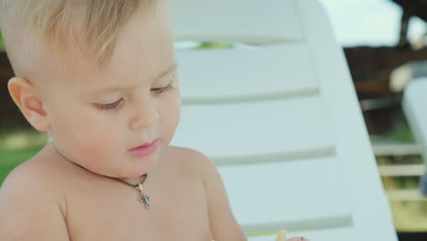 a boy of 1 year eats cookies sits on a white sunbed on the beach rest on the sea with a small child