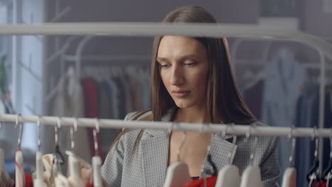 una joven morena en una tienda de ropa elige un vestido para colgar en un colgante y lo prueba. compra un vestido en la tienda. busca y elige ropa en una boutique. toma el vestido del colgante en el soporte