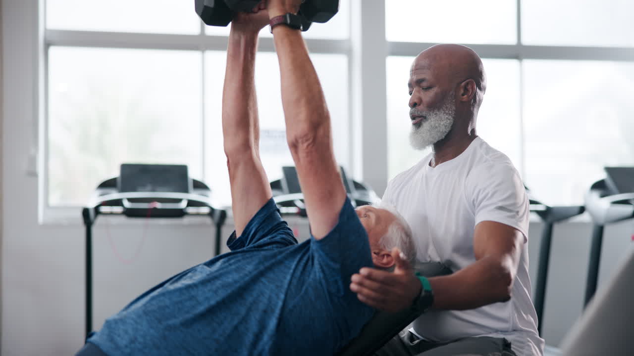 Older men working out with dumbbells and a personal trainer in a gym