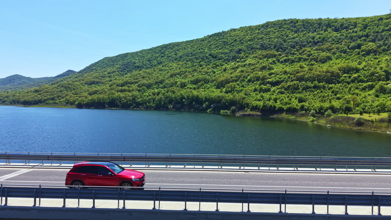 夏の晴れた日、道の近くにある澄んだ湖が緑の丘を映している。