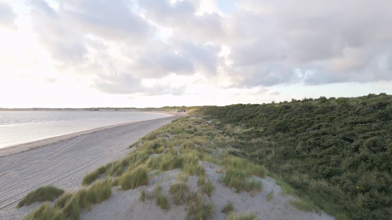 Luftaufnahme eines Vorwärtsflugs über Dünengras und Sandstrand in den Niederlanden bei Sonnenaufgang.