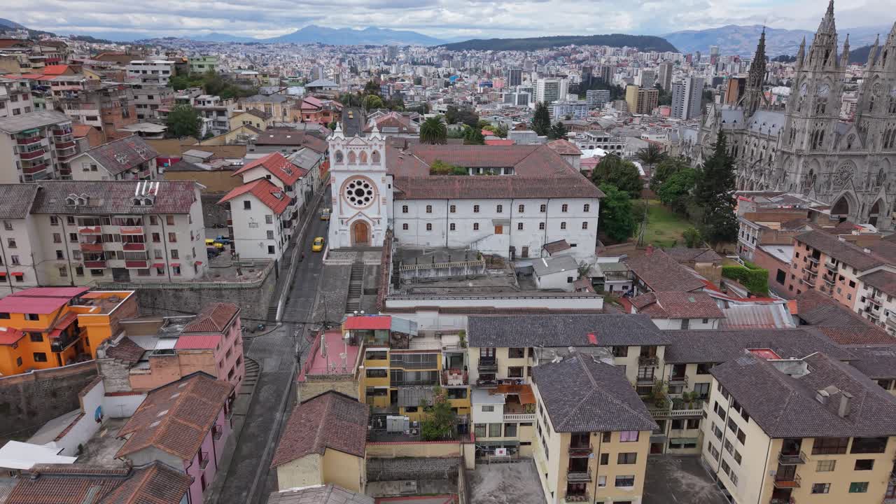 Vista de dron alejándose del Monasterio de La Encarnación de San Juan con la Basílica del Voto Nacional visible al fondo, centro histórico de Quito, Ecuador.