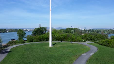 Pedestal-drone-shot-of-a-windmill-standing-in-the-middle-of-a-park-in-Danube-Island-in-Vienna,-Austria