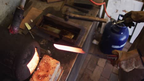 close up hands of caucasian male knife maker in workshop using oven and making knife