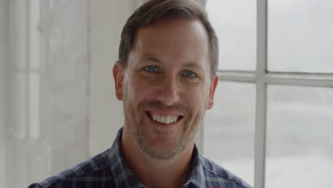 Retrato-De-Un-Joven-Caucásico-Sonriendo-Alegre-Satisfacción-Mirando-La-Cámara-Disfrutando-De-Un-Estilo-De-Vida-Exitoso-De-Pie-Junto-A-La-Ventana