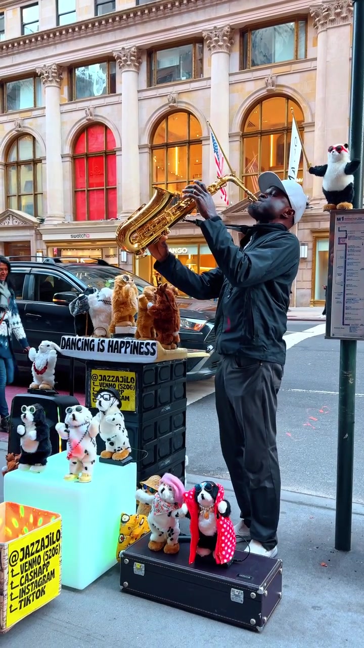 New York, USA, 5 ottobre 2025: Artista di strada con sassofono e esposizione di giocattoli danzanti. Ampia inquadratura di un musicista che suona il sassofono circondato da numerosi peluche danzanti su un marciapiede di New York.