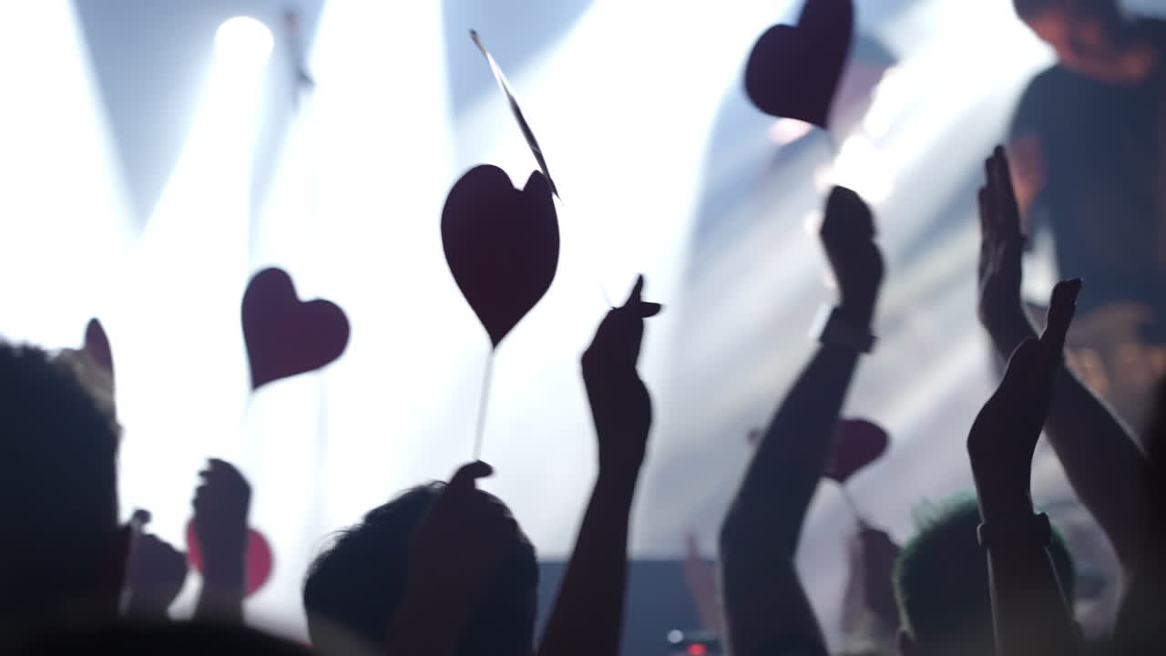 Audience at concert holding heart-shaped signs with vibrant lights creating an energetic atmosphere