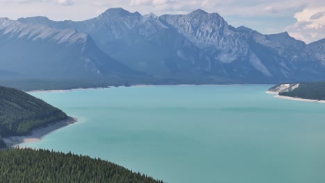 The-blue-green-waters-of-Abraham-Lake-as-seen-from-a-drone-as-it-flies-right-to-left-across-the-forest-of-the-Rocky-Mountains-of-Alberta,-Canada