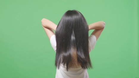 back view of a woman using her hands flipping her long black and blond straight healthy hair in the green screen background studio