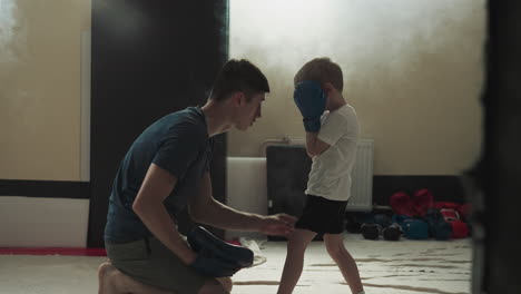 instructor teaches child boxing in sports gym. careful combat trainer explains right posture to little boy in fighting club slow motion. children lesson