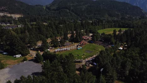 Aerial-view-of-a-grass-field-surrounded-by-mountains,-trees-and-residential-areas-in-Squamish,-BC
