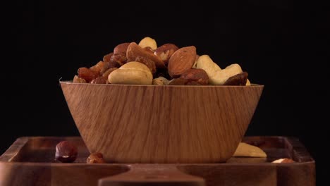 view of wood bowl full of variety of nuts on black background