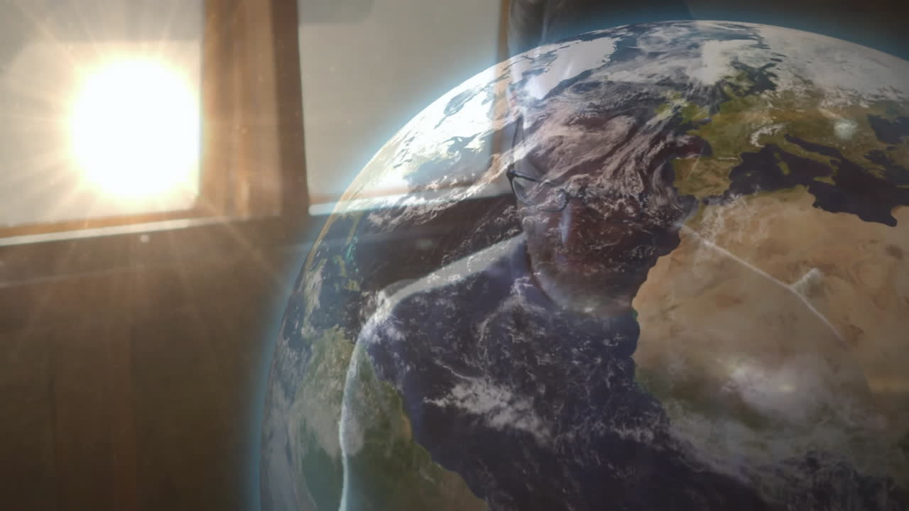 Mature man wearing eyeglasses and earbuds, viewing Earth globe overlay during technology webinar