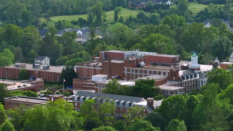 american school with red brick and waving american flag during sunny day. aerial wide shot. proud country with historic townhouses in foreground. aerial wide shot.