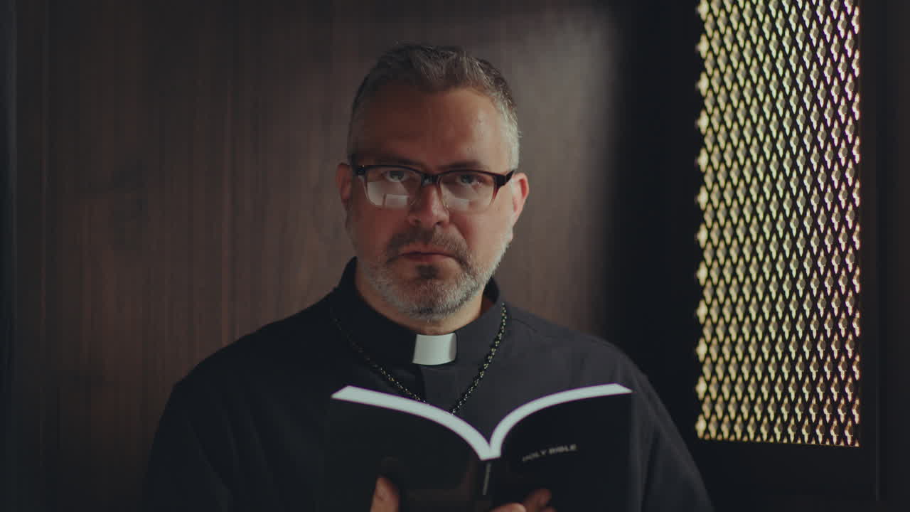 Portrait of Catholic Priest Holding Bible in Confessional Booth