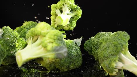 broccoli florets drop onto a black surface, creating a dynamic splash effect under bright lighting
