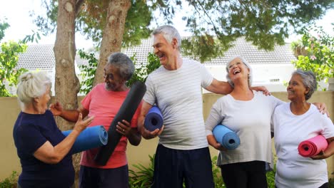 Smiling-senior-friends-holding-exercise-mat-and-interacting-with-each-other-4k