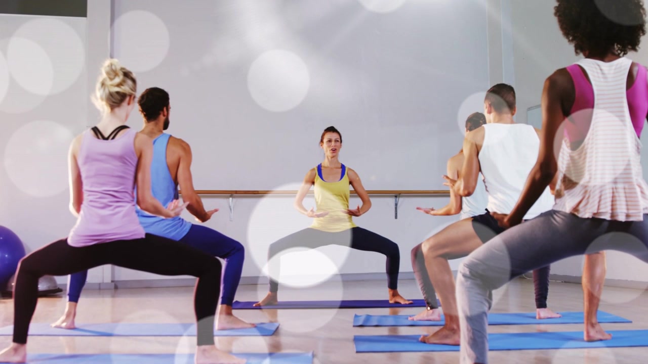 Instructor cueing fitness class, students holding squat, lifting arms for posture, bokeh over class