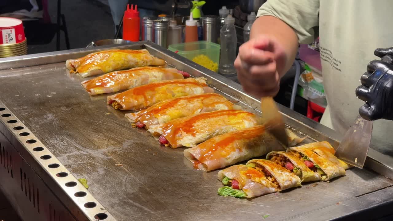 A close-up of a vendor cutting up crispy popiah and pancake rolls on a hawker street food stall in Penang, Malaysia