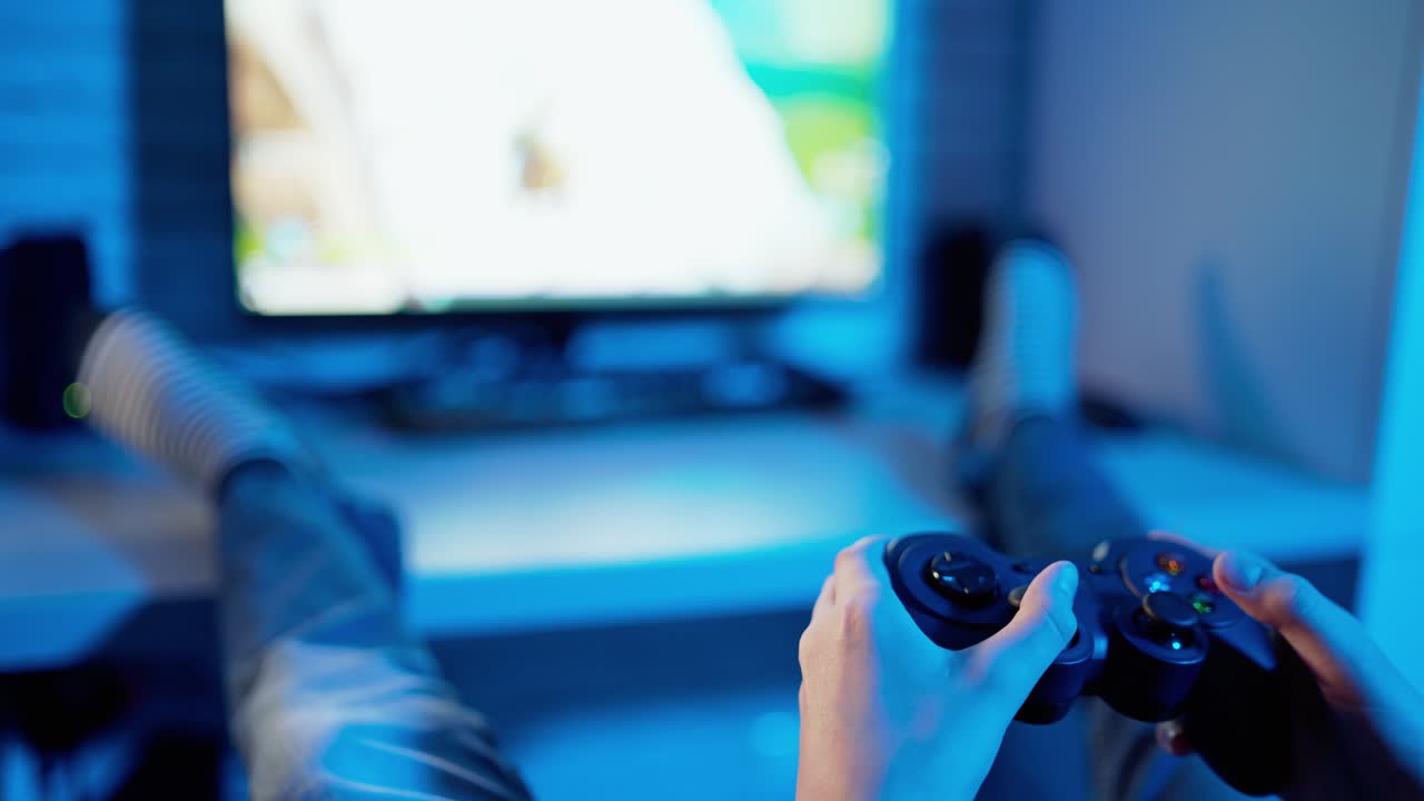 Young gamer playing video game using controller. Joystick in boy's hands in front of the play station screen. Close-up. Blue light.