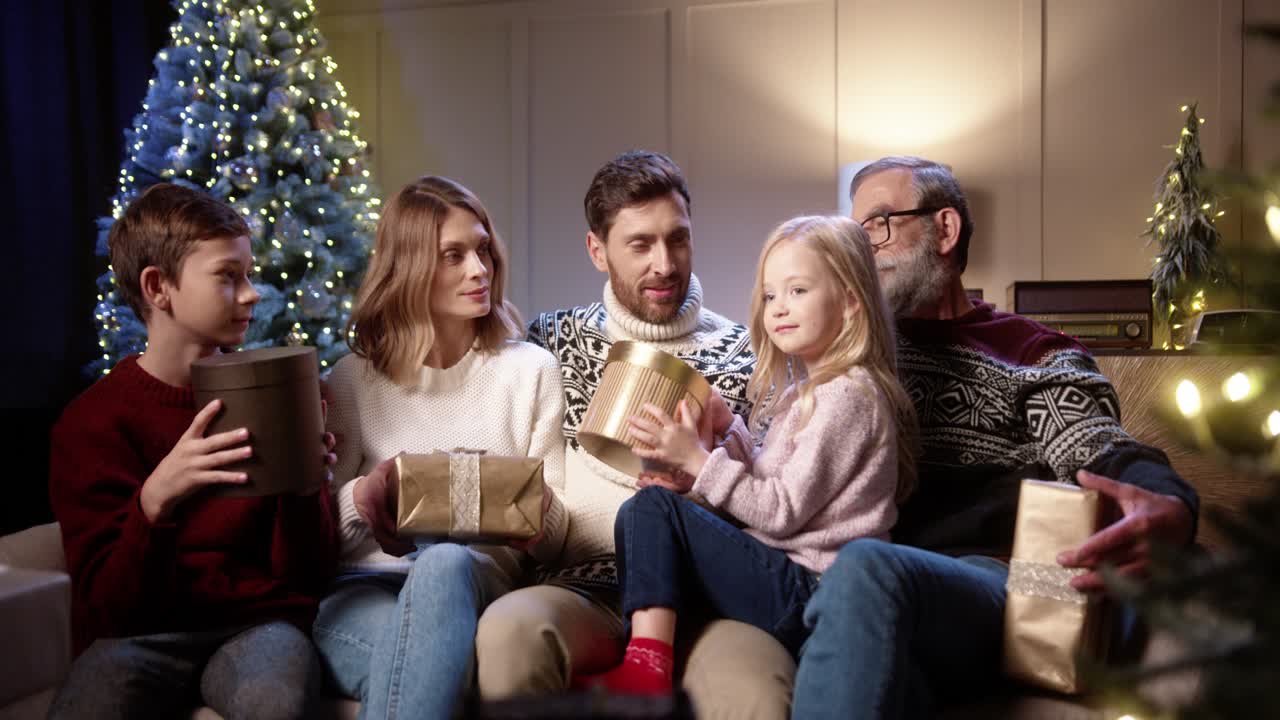 Cheerful Family With Kids Sitting Together At Cozy Home Near Decorated Christmas Tree Smiling And Giving Xmas Gifts And Presents To Each Other On New Year Eve