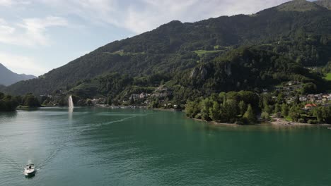 Aerial-view-of-a-boat-on-the-water-of-a-blue-green-lake-near-a-small-mountain-village-in-Switzerland