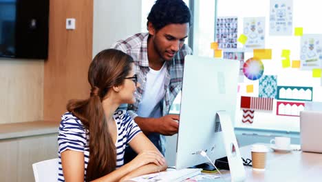 Male-and-female-executives-discussing-over-computer-at-desk