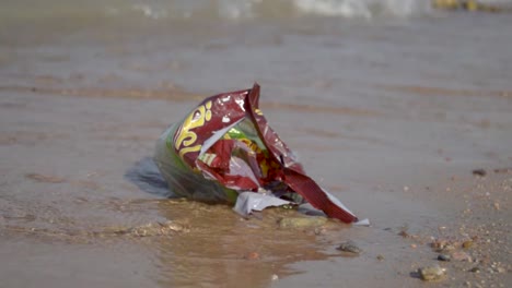 paquete de bocadillos de plástico vacío dejado en la playa moviéndose en ondas suaves, parte 1, todavía