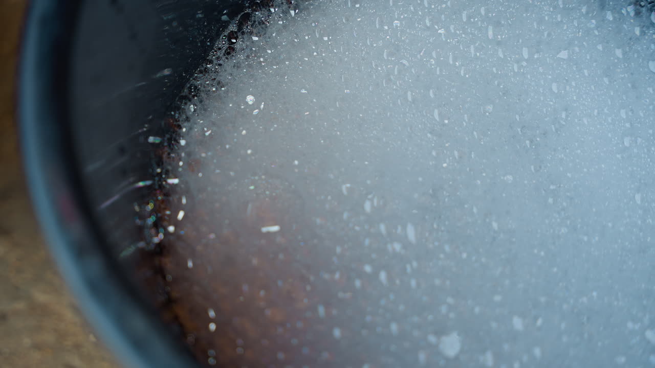 Secchio nero con schiuma e bolle, primo piano di acqua saponata che mostra la densa texture della schiuma e piccoli riflessi. Una scena di pulizie domestiche che evoca faccende tranquille, secchio appoggiato sul pavimento, schiuma delicata.