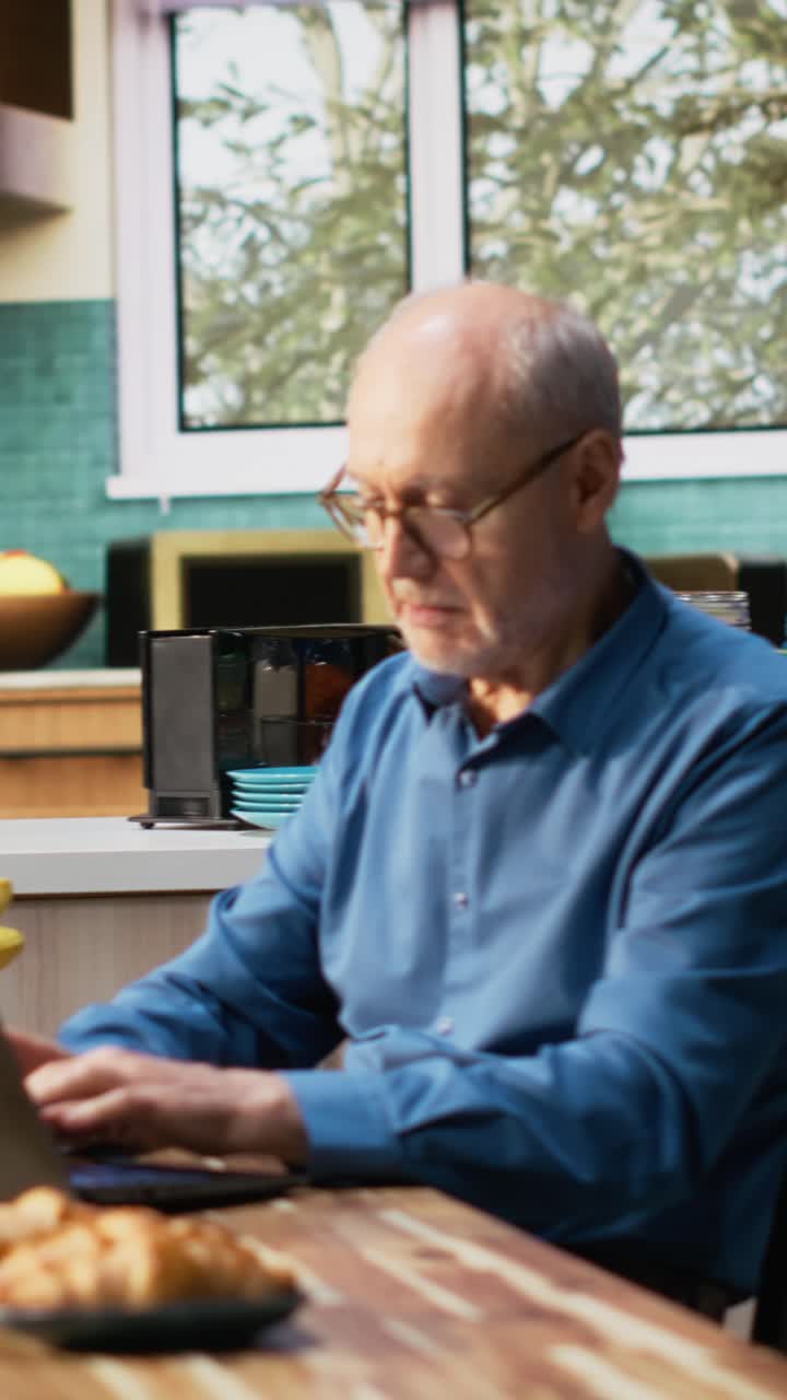 Vertical Video Mature old man browsing internet on laptop in a calm kitchen moment