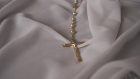 close up of gold rosary with pearl beads resting on soft white fabric in natural light