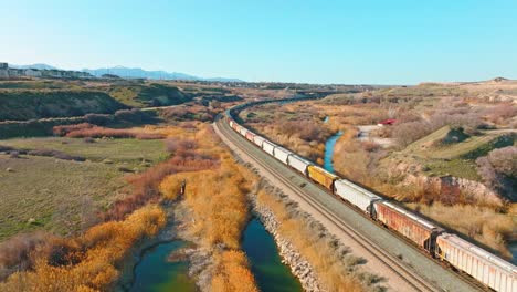 AERIAL---Train-on-railroad-tracks-close-to-Bluffdale,-Utah,-forward-lowering-shot