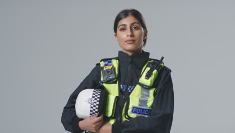 studio portrait of serious young female police officer holding helmet against plain background