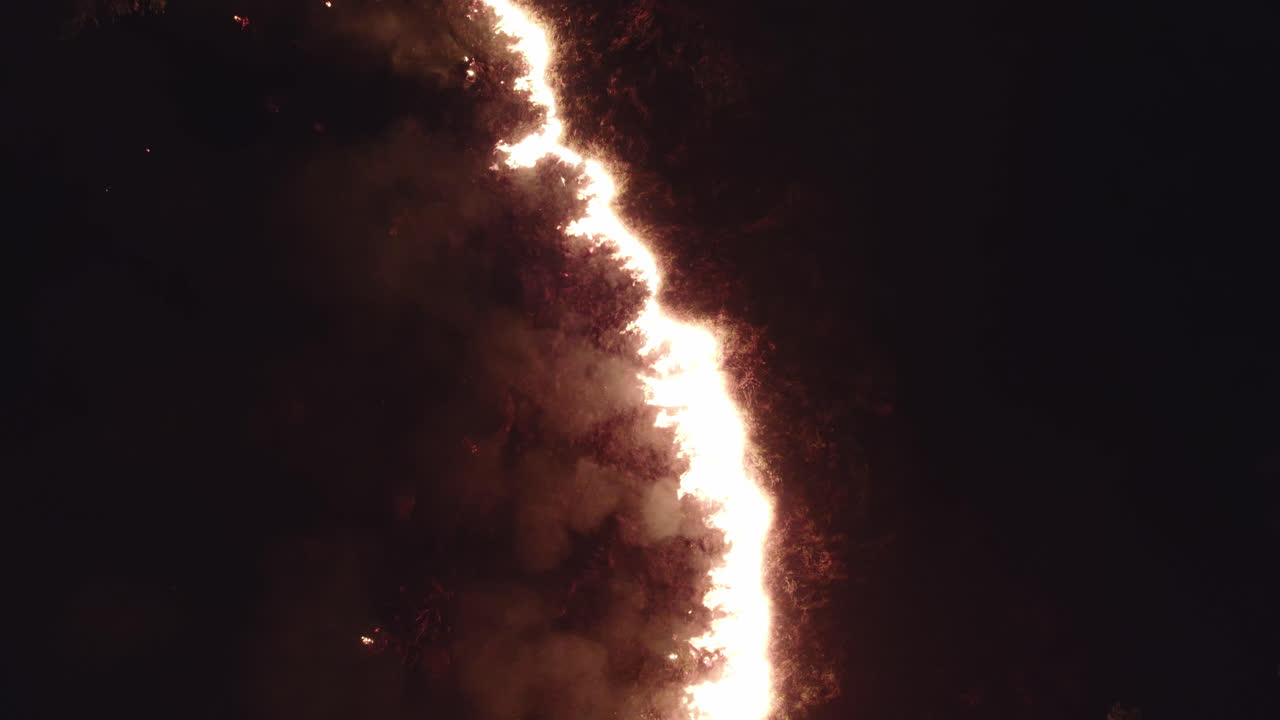 Fire spreding through vegetation at night, flames up high creating a vertical division