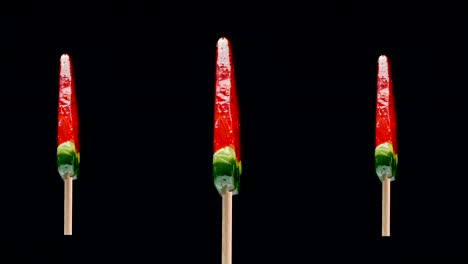 una piruleta roja está girando sobre un fondo negro, una piruleta de sandía y caramelo. dulces para niños.