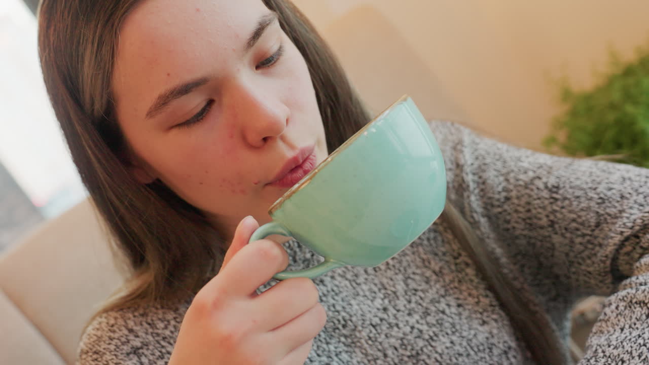 Close up female staff taking lunch in canteen holding empty turquoise cup after finishing hot drink relaxed posture cozy ambiance background with greenery detail casual attire suggests comfort