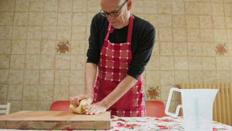 bald man handles and rolls out raw dough in the kitchen