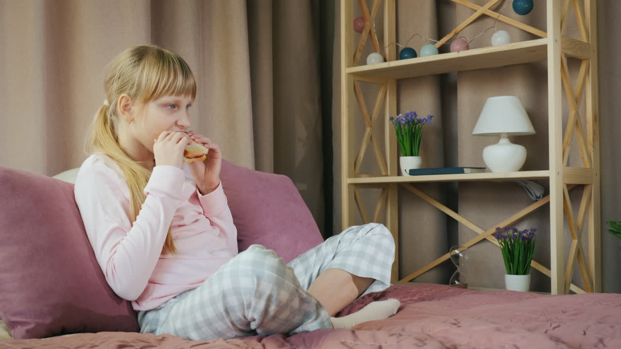 아이는 샌드위치를 먹고 침대에 앉아 tv를 본다